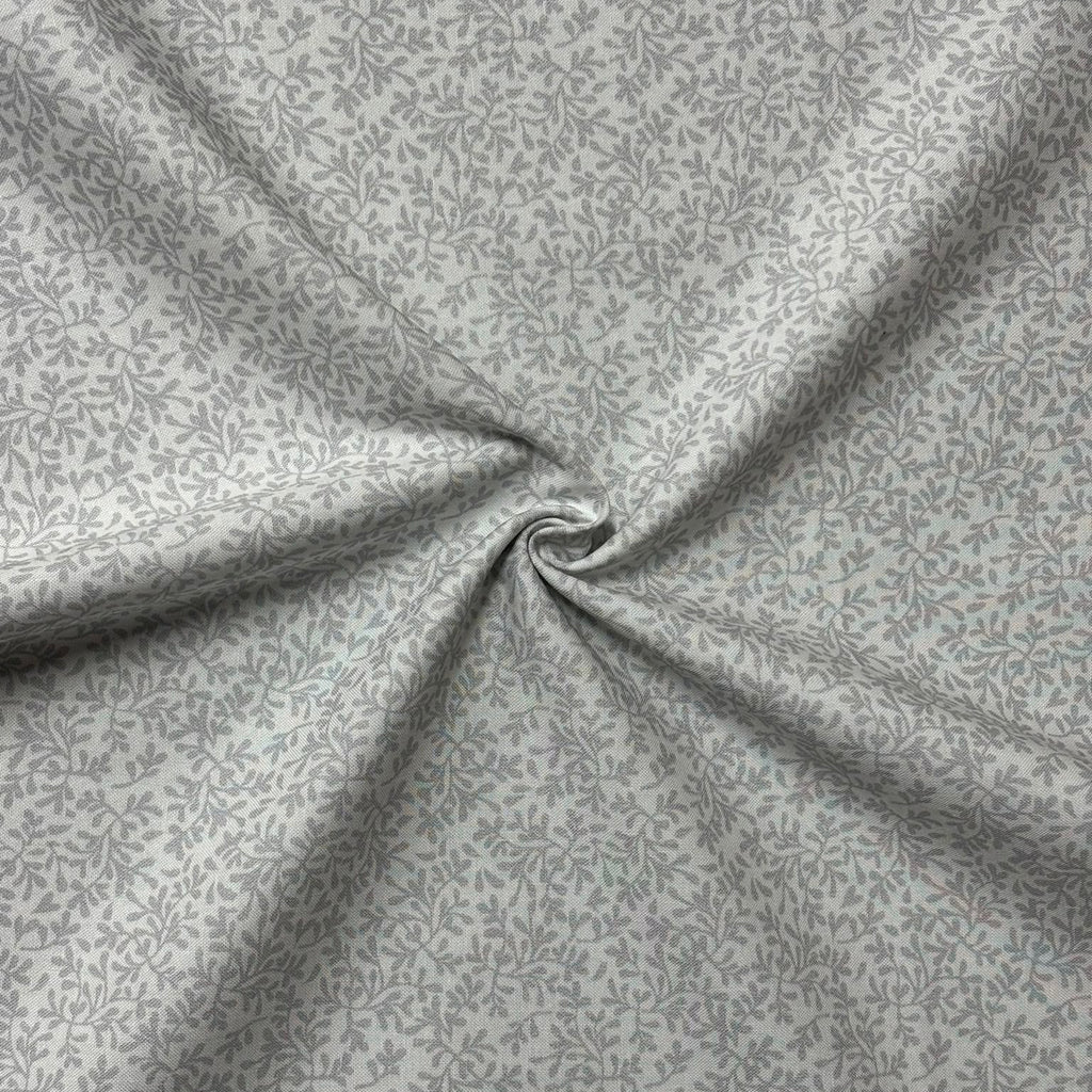 A close-up of white fabric with a dense, small-scale leafy or floral pattern, arranged in a central swirl to show its drape and texture.